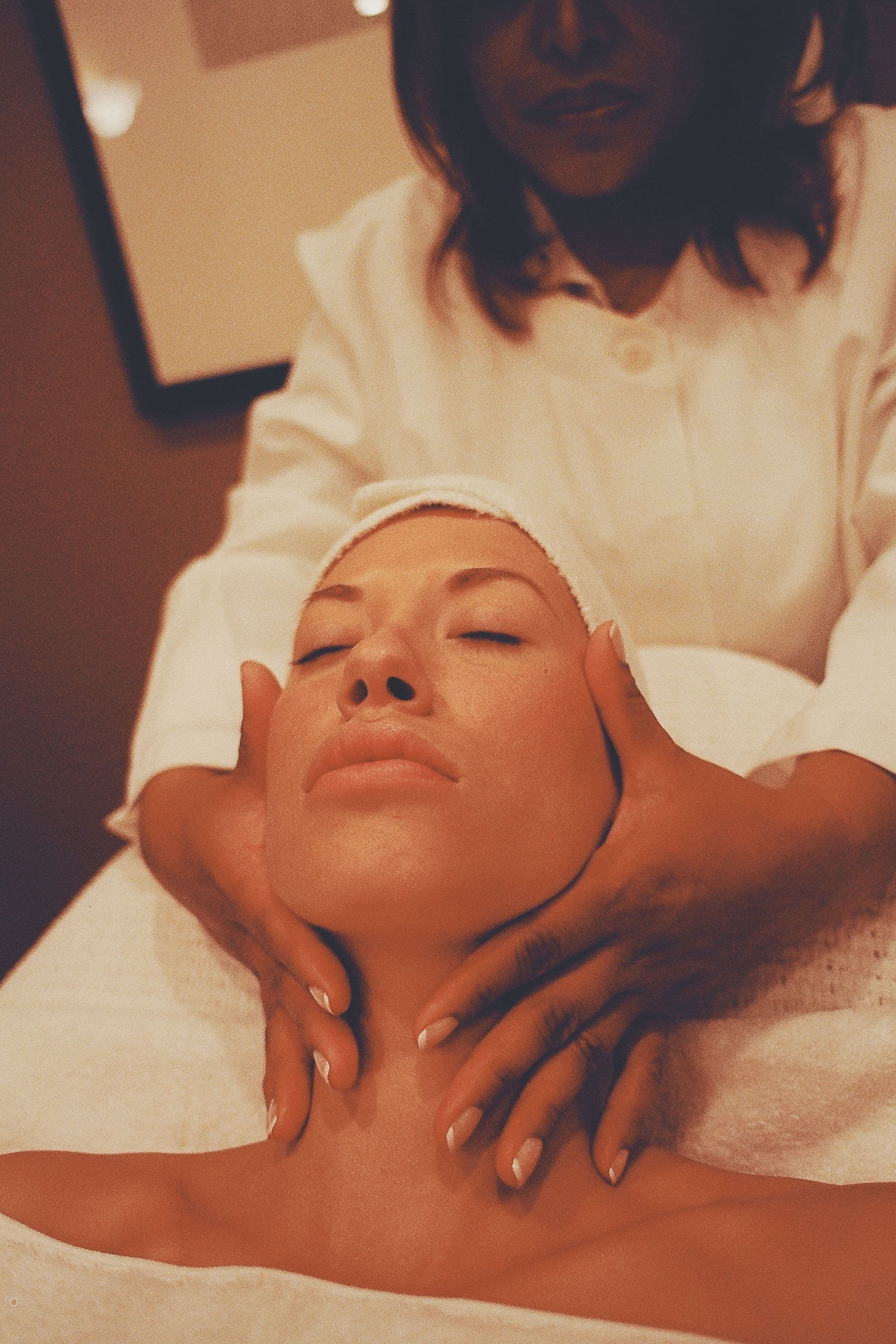 A therapist massaging a guest's face and neck, a towelling headband holding her hair back