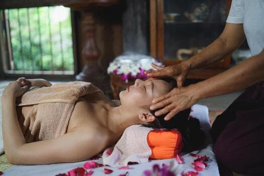 A therapist working across a guest's forehead and temples, rose petals scattered on the table