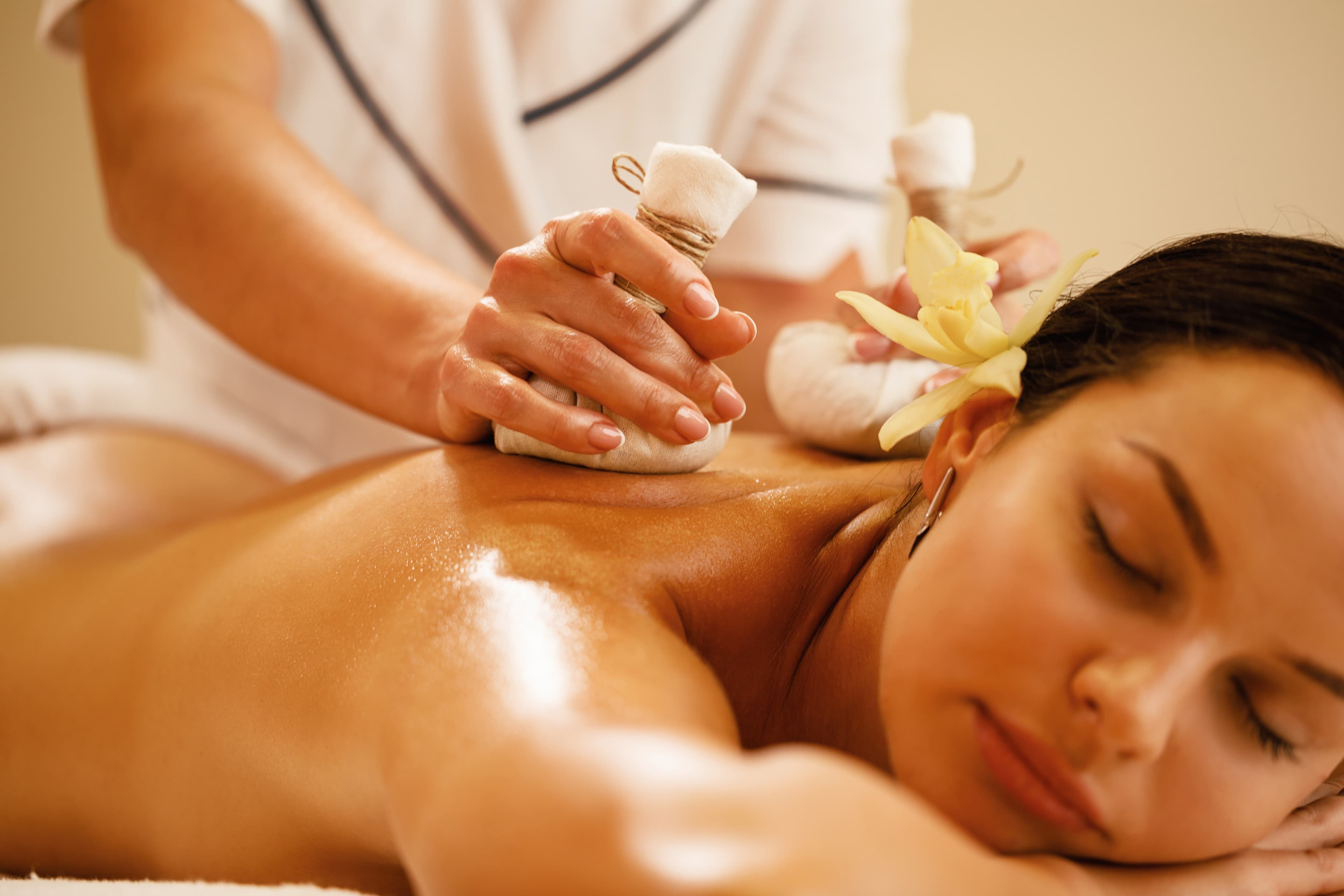 A therapist pressing warm cloth-tied herbal poultices along an oiled back